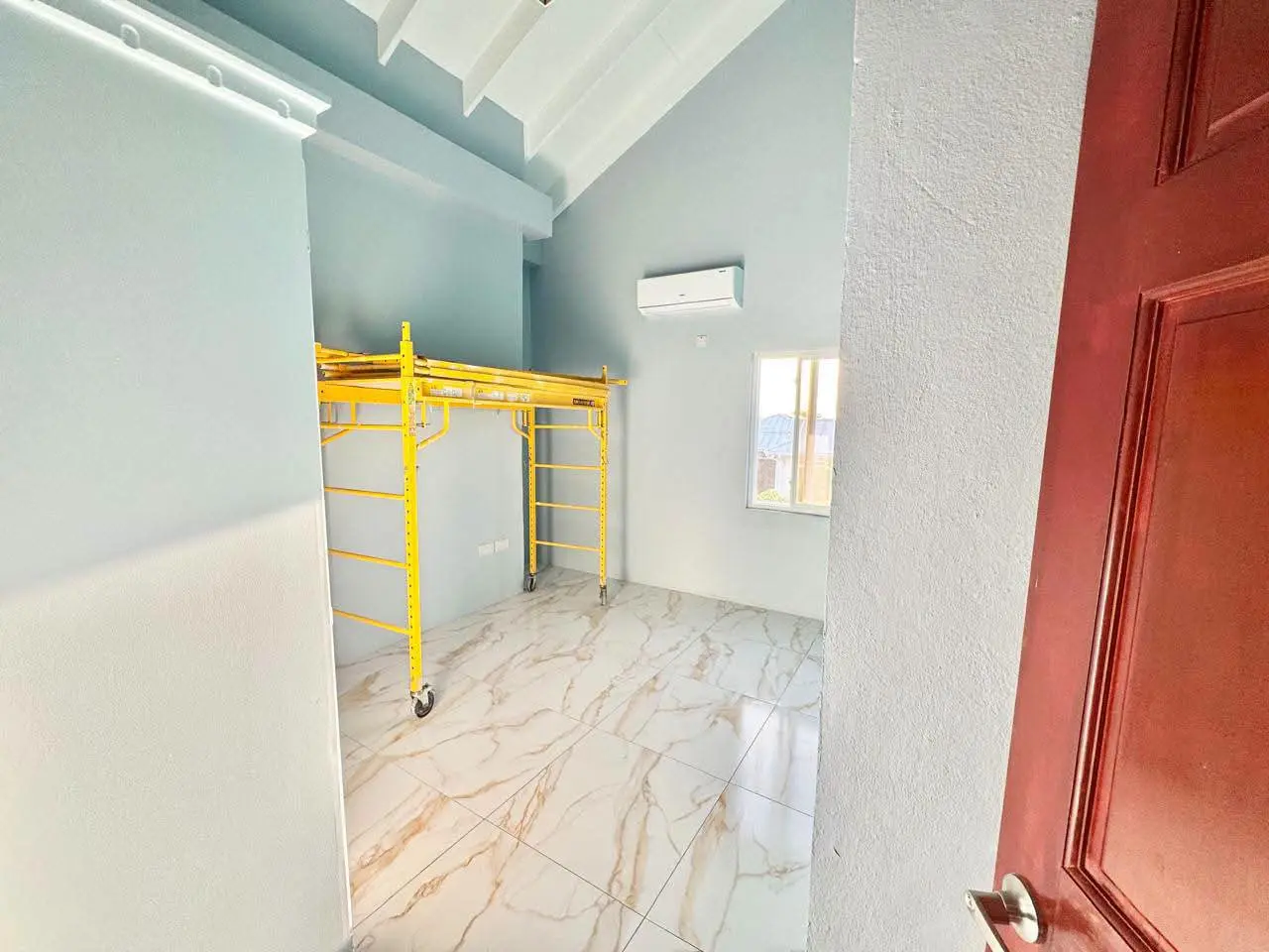 Interior room with light blue walls, marble-design porcelain floor tiles, wall-mounted split air conditioning unit and yellow scaffolding still in place, Saint Lucia