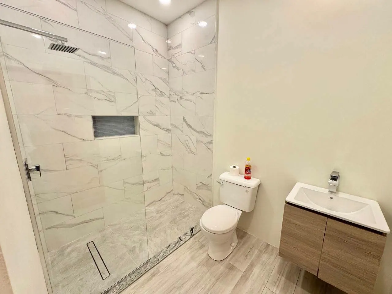 Modern bathroom featuring full-height marble-design wall tiles, frameless glass shower enclosure with rain head, wall-hung vanity unit and chrome fixtures, Saint Lucia