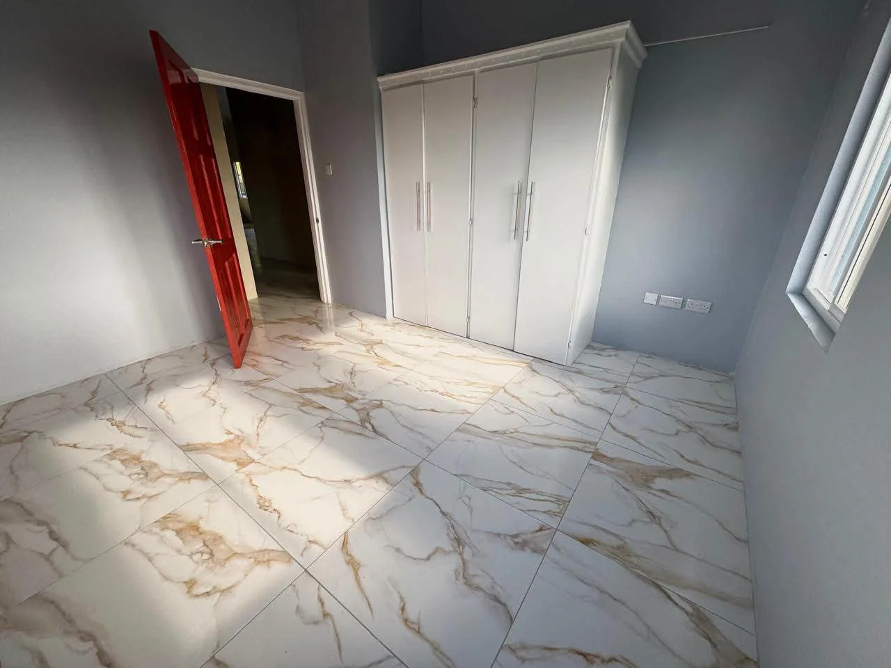 Bedroom with charcoal grey walls, built-in white four-door wardrobe with chrome bar handles and polished marble-design gold-veined porcelain floor tiles, Saint Lucia