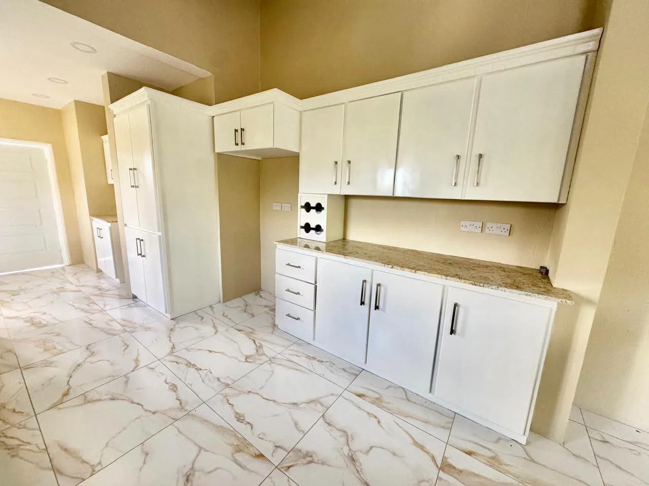 Spacious modern kitchen with full-height white shaker-style upper and lower cabinetry, granite countertops, marble-design porcelain floor tiles and recessed ceiling lighting, Saint Lucia
