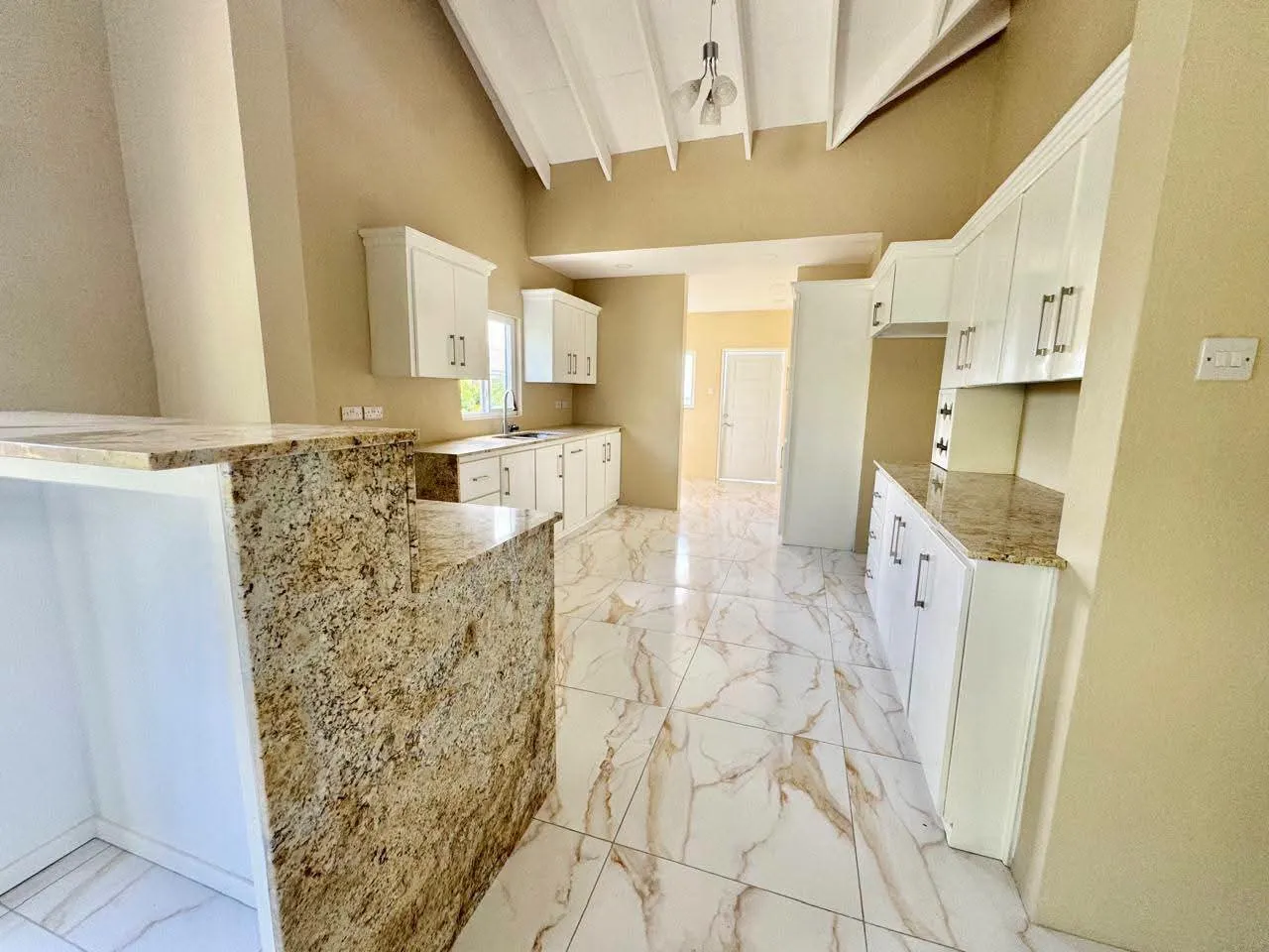 Open-plan kitchen with vaulted beamed ceiling, large granite-top island breakfast bar, white shaker cabinets, pendant lighting and polished marble-design tile flooring, Saint Lucia